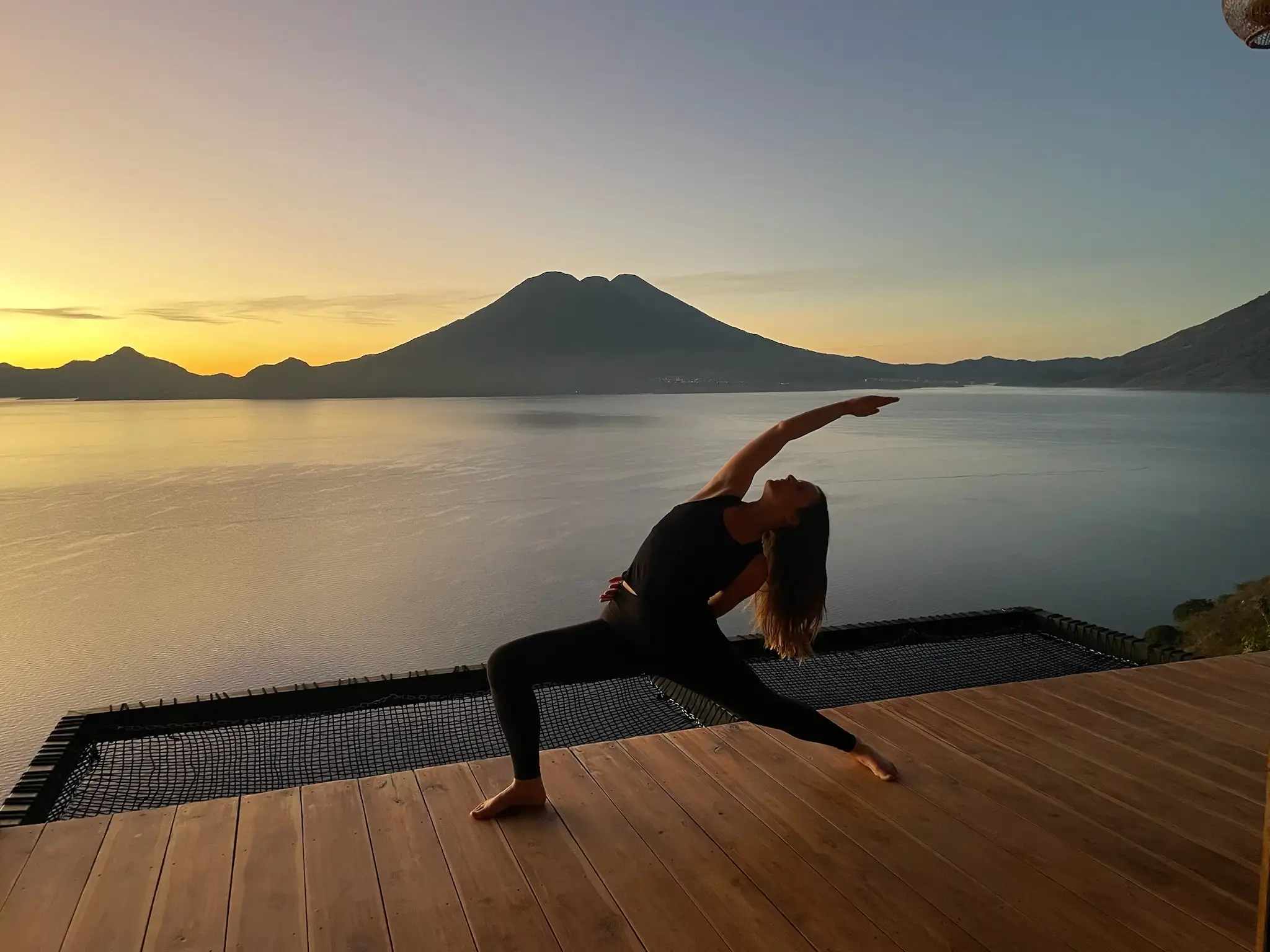 Michaela in a warrior asana on a deck overlooking a lake at sunrise